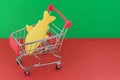 Shopping basket on a red and green background with a plastic fish inside. The concept of unnatural products with harmful additives