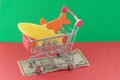 A shopping basket on a red and green background with plastic fish stands on a banknote. The concept of unnatural products with