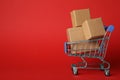 Shopping cart with boxes on red background. Logistics and wholesale concept