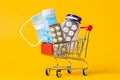 A shopping cart filled with medicines and a medical mask. Yellow background. Close up. The concept of buying medicines Royalty Free Stock Photo