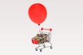 Shopping cart full of coins and red balloon floating on white background Royalty Free Stock Photo