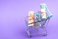 Shopping cart full of roll euro banknotes on purple Royalty Free Stock Photo