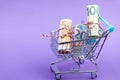 Shopping cart full of roll euro banknotes on purple