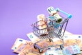 Shopping cart full of roll euro banknotes on purple Royalty Free Stock Photo