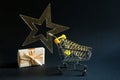 Shopping cart with a gold transparent star with sequins in the shape of a Christmas tree on a black background. Black Friday, buyi