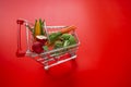 Shopping cart with groceries on a red background.grocery consumer basket.food cost.Vegetables and fruits price increase Royalty Free Stock Photo