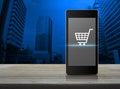 Shopping cart icon on modern smart phone screen on wooden table Royalty Free Stock Photo