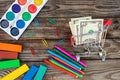 Shopping cart with money. Office and school supplies on old wooden background.