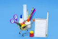 Shopping cart with pencil, eraser, sharpener, gouache paint, notepad, sticky tape. Material list and back to school concept Royalty Free Stock Photo