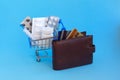 A shopping cart with pills, and syringe next to a purse with credit cards on blue background Royalty Free Stock Photo