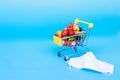 Shopping cart with medical mask with fruits and vegetables on a blue background. online shopping on quarantine concept