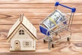 Shopping cart with rolled up dollar bills and model of house on the wooden background Royalty Free Stock Photo