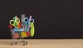 Shopping cart with school supplies over chalkboard background Royalty Free Stock Photo