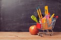 Shopping cart with school supplies over chalkboard background Royalty Free Stock Photo