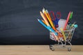 Shopping cart with school supply in front of blackboard. Back to school concept. Royalty Free Stock Photo