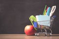 Shopping cart with school supply in front of blackboard. Back to school concept