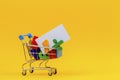 Shopping cart or supermarket trolley full of colorful numbers and white card on yellow background Royalty Free Stock Photo