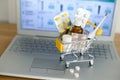 Shopping cart toy with medicaments in front of laptop screen with pharmacy web site on it. Pills, blister packs, medical bottles,