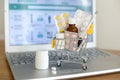 Shopping cart toy with medicaments in front of laptop screen with pharmacy web site on it.