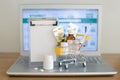 Shopping cart toy with medicaments and paper note in front of laptop screen with pharmacy web site on it.