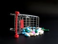 Shopping carts overthrow colorful medicine on black background.