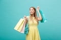 Shopping Concept: Portrait of an excited beautiful girl wearing yellow dress holding shopping bags isolated over blue Royalty Free Stock Photo