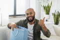 Shopping and delivery concept. Excited latin man opening shopper bag delivered from clothing shop and gesturing thumb up