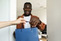 Shopping delivery. Female courier giving shopper bags to black male customer standing in doors of his home Royalty Free Stock Photo