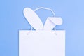 Shopping for Easter. White paper shopping bag with white bunny ears on blue background. Concept Easter gifts Royalty Free Stock Photo