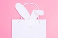 Shopping for Easter. White paper shopping bag with white bunny ears on pink background. Concept Easter gifts Royalty Free Stock Photo