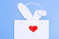 Shopping for Easter. White paper shopping bag with white bunny ears and a red heart as a nose on a blue background Royalty Free Stock Photo