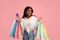 Shopping frenzy concept. Smiling black lady with gift bags and credit card buying holiday presents on pink background