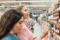 Shopping at the grocery store. Two young women brunette and blonde choose products in the store. In the background, the trading Royalty Free Stock Photo