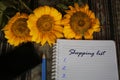 Shopping list text with numbers on notebook with sunflowers, spiral book and a pen on natural classic fabric background.