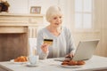 Modern pensioner shopping online while having breakfast