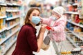 Shopping. Portrait of a young woman in a medical mask and her baby sitting in a grocery cart, wearing a medical mask. The concept Royalty Free Stock Photo