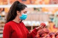 Shopping. Portrait of a young woman in a medical mask on her face choosing apples in a supermarket. The concept of consumerism and