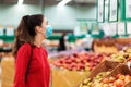 Shopping. Portrait of a young woman in a medical mask on her face looking at apples in a supermarket. The concept of shopping and