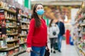 Shopping. Portrait of a young woman in a medical mask poses in the aisle of a supermarket. The concept of consumerism and the new Royalty Free Stock Photo