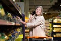 Shopping in the store. Senior beautiful woman walks in the store, supermarket between the rows, talks on the phone, consults, with Royalty Free Stock Photo