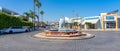 Shopping street in Ayia Napa in Cyprus with roundabout with fish figure monument and a parked white limousine
