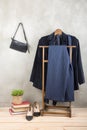 Shopping and style concept - clothes rack with trendy blue jacket and striped pants, bag and shoes on wooden floor and grey Royalty Free Stock Photo