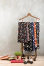 Shopping and style concept - clothes rack with trendy dresses in floral print, shoes and books on wooden floor and grey concrete Royalty Free Stock Photo