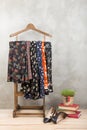 Shopping and style concept - clothes rack with trendy dresses in floral print, shoes and books on wooden floor and grey concrete Royalty Free Stock Photo