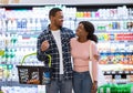 Shopping together. Happy black couple hugging and looking at each other at mall, purchasing food with grocery basket Royalty Free Stock Photo