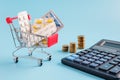 Shopping trolley cart filled medicinal tablets, stacks of coins in row on blue background