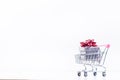 Shopping trolley with christmas gift. Gift box with red ribbon on a white background. Christmas decoration. Royalty Free Stock Photo