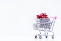 Shopping trolley with christmas gift. Gift box with red ribbon on a white background. Christmas decoration. Royalty Free Stock Photo