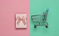 Shopping trolley, gift box on pink-blue pastel background. Top view Royalty Free Stock Photo