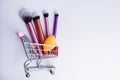 Shopping trolley with make-up products and brushes over white background